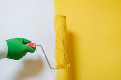 Man holds roller brush with yellow paint over yellow half painted wall