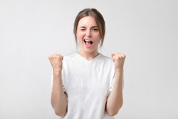 Beautiful lucky european girl feeling excited and happy after she won lottery unexpectedly or passing diffficult exam in college, keeping mouth opened and fists up