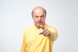Portrait of serious senior man with warning finger and yellow t-shirt shirt against light gray background. You better listen to my advice concept