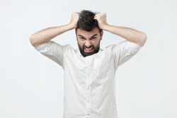 Angry and furious man on a gray background. He pulls out his hair in a rage