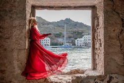 View of Balaklava Bay through an arched balcony in oriental style. The girl in a long red dress stands with her back. Abandoned mansion on the Black Sea coast