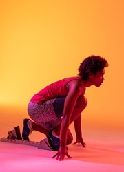 Vertical image of african american female athlete preparing for run in yellow lighting. Sport, movement, fitness and active lifestyle concept.