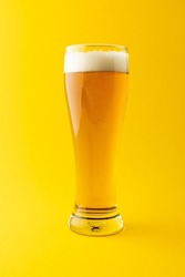 Vertical image of full pint glass of lager beer on yellow background, with copy space. Drinking alcohol, refreshment and lager day celebration concept.