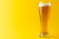 Image of full pint glass of lager beer, with copy space on yellow background. Drinking alcohol, refreshment and lager day celebration concept.