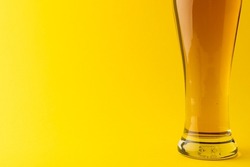 Horizontal image of pint glass of lager beer on yellow background, with copy space. Drinking alcohol, refreshment and lager day celebration concept.