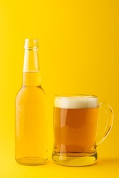 Image of full clear glass bottle and glass tankard of lager beer, with copy space on yellow. Drinking alcohol, refreshment and lager day celebration concept.
