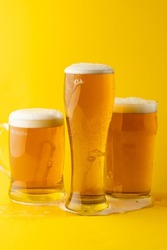 Image of three different full pint glasses of lager beer, with copy space on yellow background. Drinking alcohol, refreshment and lager day celebration concept.