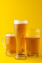 Image of three different pint glasses of lager beer, with copy space on yellow background. Drinking alcohol, refreshment and lager day celebration concept.