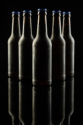 Vertical image of five dark glass bottles of lager beer with blue caps on black, with copy space. Drinking alcohol, refreshment and lager day celebration concept.