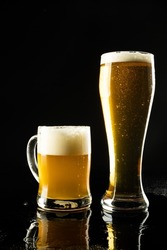 Vertical image of pint glass and glass tankard of lager beer on black background, with copy space. Drinking alcohol, refreshment and lager day celebration concept.