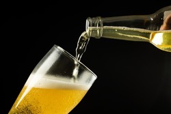Horizontal image of clear bottle of lager beer pouring into glass on black, with copy space. Drinking alcohol, refreshment and lager day celebration concept.