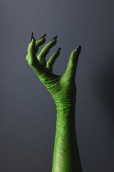 Vertical image of green monster hand with black nails with hold gesture on grey background. Halloween, tradition and celebration concept.
