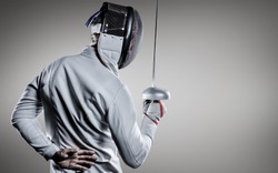 Man wearing fencing suit practicing with sword against grey vignette