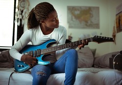 Young girl playing electric guitar in her bedroom