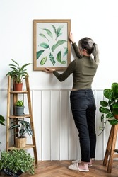 Young woman hanging a frame of leaf print painting on the wall