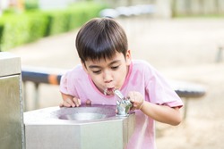 Little boy drinking water in the public park