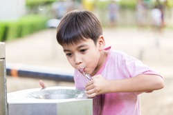 Little boy drinking water in the public park