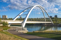 North side view to new Walterdale arch bridge across the North Saskatchewan River in Edmonton, Alberta, Canada in day light with blue sky and clouds.