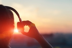 Girl in headphones listening to music in the city at sunset.