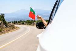 Woman holding Portugal flag from the open car window driving along the serpentine road in the mountains. Concept