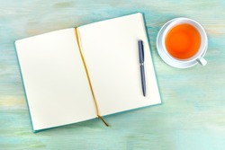 An overhead photo of an open journal notebook with a pen and a cup of tea, shot from above, a diary on a teal blue background with a place for text