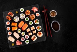 Large sushi set, shot from the top on a black background. An assortment of various maki, nigiri and rolls with sake, soy sauce, and chopsticks