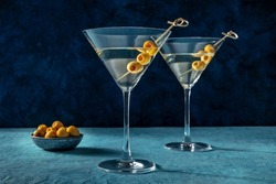 Martini, two glasses with spicy olives. Alcoholic cocktail on a blue background