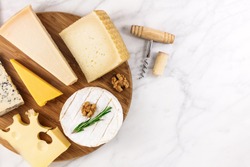 An overhead photo of a selection of cheeses, shot from above on a white marble table, with a wine corkscrew and a cork, and a place for text
