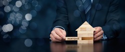 Mortgage concept. Financial agent complete wooden model of the house with last piece with text mortgage. Wide banner composition with bokeh background.