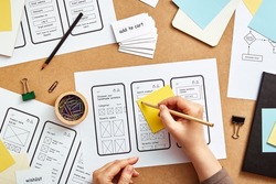 Web UX designer working on mobile responsive website. Top view image of numerous app wireframe sketches and user flow over product designer desk. 