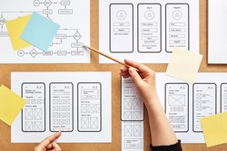 Web UX designer working on mobile responsive website. Flat lay image of numerous app wireframe sketches and user flow over product designer desk. 