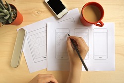 Designer drawing mobile application wireframe on wooden desk. Flat lay