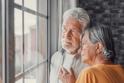 Pensive elderly mature senior man in eyeglasses looking in distance out of window, thinking of personal problems. Old woman wife consoling and hugging sad husband, copy space
