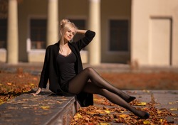 Beautiful blonde woman with perfect legs in pantyhose posing outdoor at the autumn street in the lights of the setting sun.