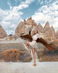 Beautiful girl with perfect legs in a traditional american fringed jacket posing in Cappadocia mountain canyon. Desert landscape with flying swallows.