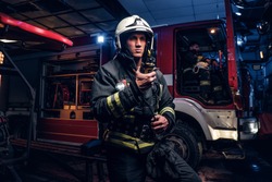 The fire brigade arrived at the night-time. Fireman in a protective uniform standing next to a fire truck and talking on the radio