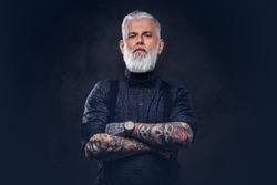Handsome hipster grandfather with tattooed hands poses in dark background looking at camera.
