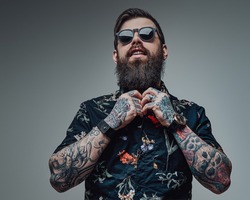 Portrait of a handsome man wearing sunglasses and black shirt in gray background. Cool guy with bearded face and tattoos.