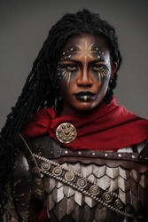 Shot of african woman warrior dressed in red cloak and steel armor isolated on gray background.