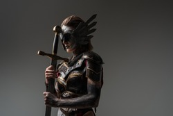 Shot of dramatic female warrior with sword dressed in steel armor posing agianst grey background.