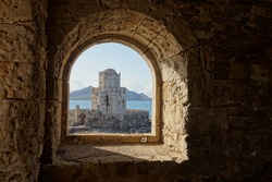 Methoni Castle in sunny weather during early morning hours with water waves in Greece viewed from a stone arch window
