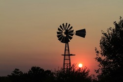 Kansas Sunset with a colorful sky and tree and Windmill  silhouettes north of Hutchinson Kansas USA out in the country.