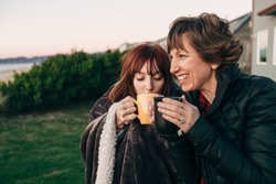 Mother and Daughter Drinking from Coffee Cups at Sunset at the Beach laughing