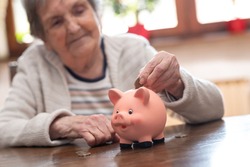 Elderly woman putting a coin in a piggy bank