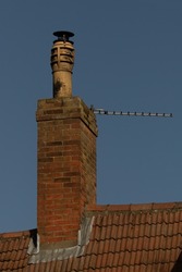 Weathered tall chimney pot on red brick chimney stack and roof against blue sky