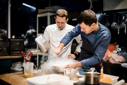 two professional male chefs preparing molecular cuisine dish in the kitchen. A lot of smoke and steam around them