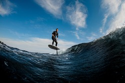 Beautiful view of man skillfully riding on the wave with hydrofoil foilboard on background of blue sky