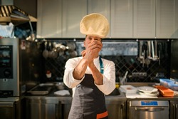 Male chef at kitchen skilfully tossing pizza dough in the air. Process of making a pizza base