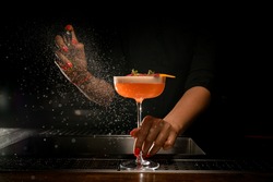 direct view of glass with bright delicious frothy cocktail that woman bartender holds with her hand and sprinkles on it. A lot of drops around