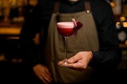 hand of bartender holds beautiful cocktail glass with tasty foamy bright pink drink and decoration